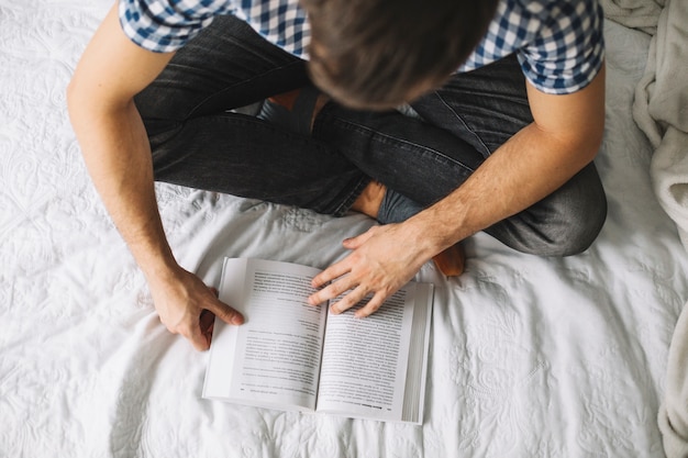 De cima homem lendo livro na cama