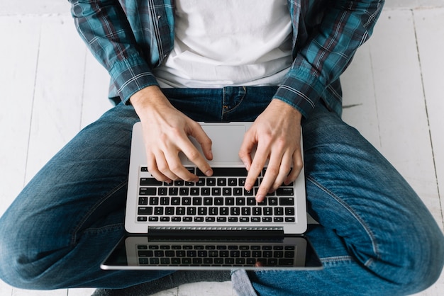 De cima homem usando laptop no chão