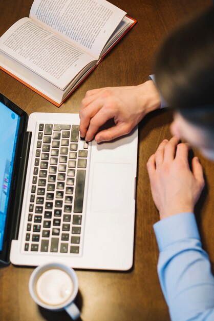 De cima homem usando laptop perto de livro