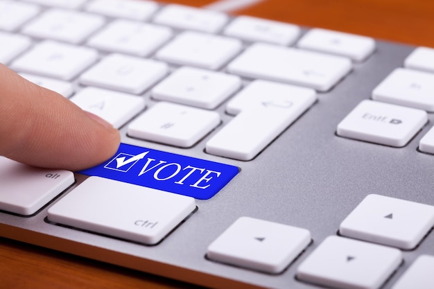 Foto grátis dedo pressionando o botão azul de votação e o símbolo no teclado. eleições online