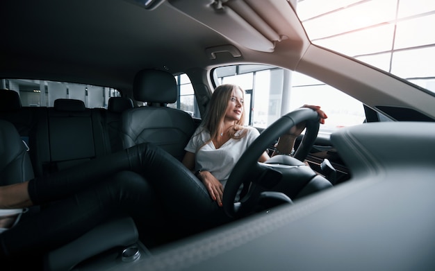 Deitado nos assentos. Garota em um carro moderno no salão. Durante o dia dentro de casa. Comprando novo veículo