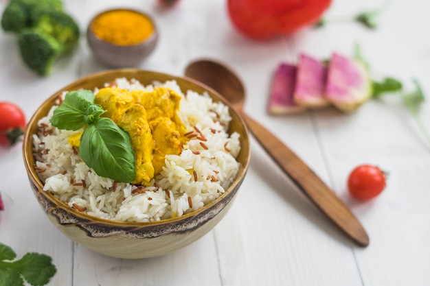 Deliciosa comida com frango na tigela perto de colher e ingredientes na mesa branca