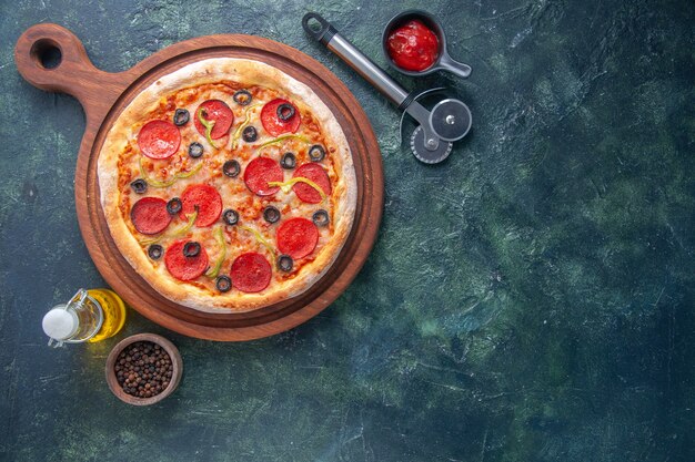 Deliciosa pizza caseira com tomate em tábua de madeira e ketchup de pimenta em garrafa de óleo no lado direito em superfície escura