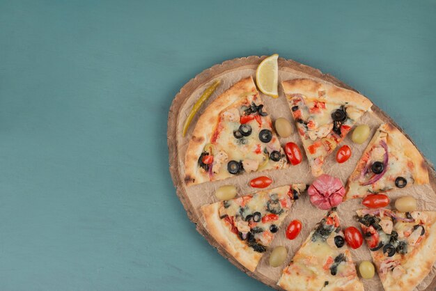 Deliciosa pizza quente com azeitonas e tomates na superfície azul.