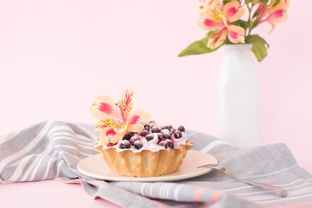 Deliciosa torta com mirtilos e alstroemeria flor na placa cerâmica contra pano de fundo-de-rosa