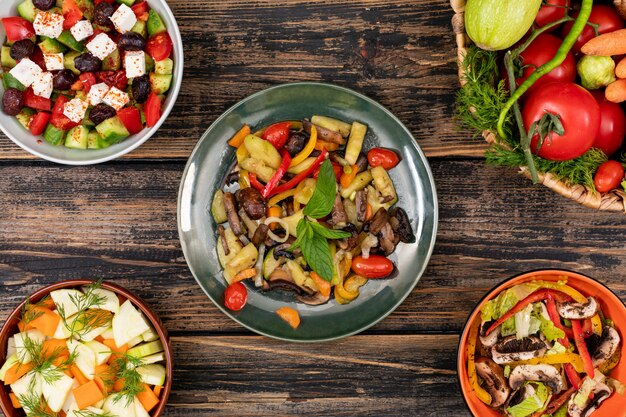 Deliciosas saladas de legumes em diferentes tigelas na vista superior de mesa de madeira