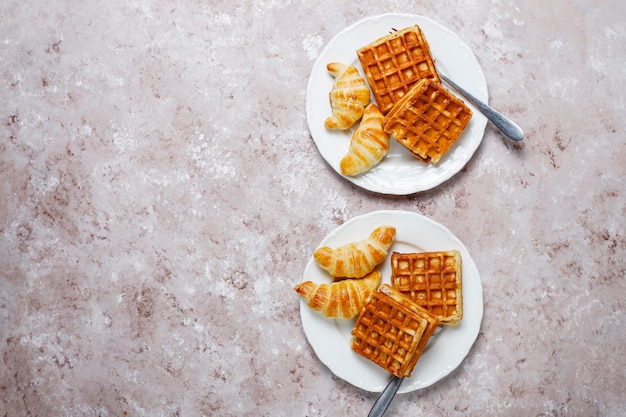 Delicioso café da manhã com café, suco de laranja, waffles, croissants, geléia, pasta de nozes na luz, vista superior