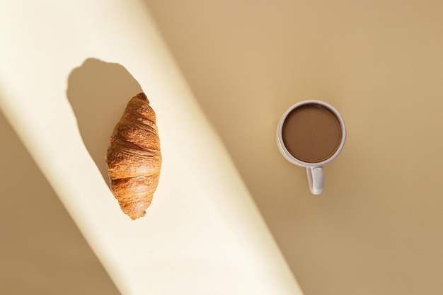Delicioso croissant e uma xícara de café com leite em bege com luz do sol café da manhã no ensolarado de verão
