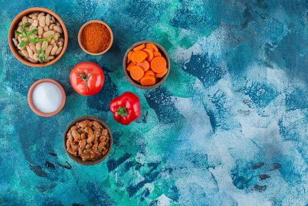 Delicioso feijão cozido em tigelas com legumes, na mesa azul.