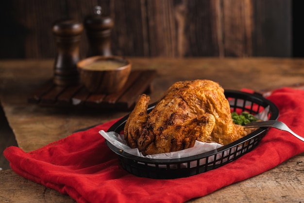 Delicioso frango assado perto de alguns temperos em uma toalha de mesa vermelha em uma mesa de madeira