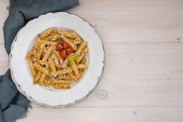 Delicioso macarrão penne com queijo ralado e tomate na placa branca cerâmica na mesa de madeira