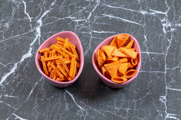 Delicioso palito crocante e chips triangulares em tigelas cor de rosa.