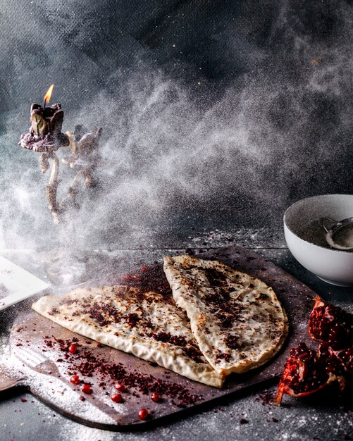 Delicioso prato de carne e abóbora Qutabs derramado com farinha com fatias de romã e sumax na superfície cinza