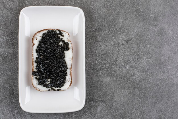 Delicioso sanduíche com caviar preto em prato branco sobre superfície cinza