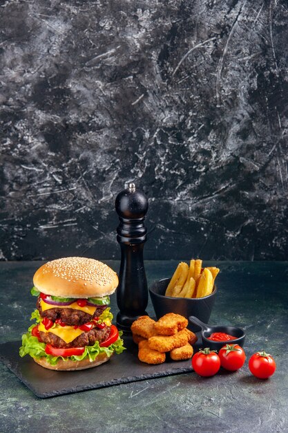 Delicioso sanduíche e nuggets de frango fritas na bandeja de tomate de cor escura na superfície preta em visualização vertical