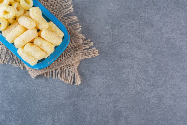 Deliciosos anéis de milho em uma placa de madeira com textura, na superfície de mármore.