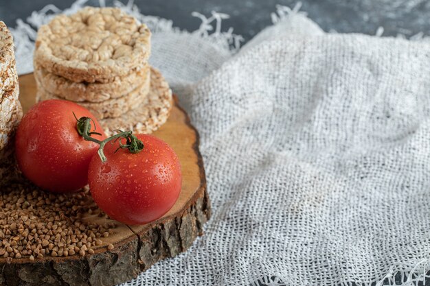 Deliciosos bolos de arroz, tomates e trigo sarraceno cru na peça de madeira