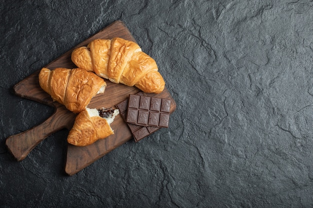 Deliciosos croissants com saborosas barras de chocolate em uma placa de madeira.