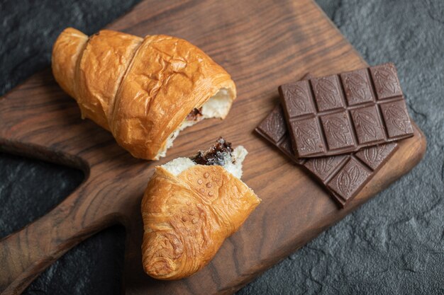 Deliciosos croissants com saborosas barras de chocolate em uma placa de madeira.