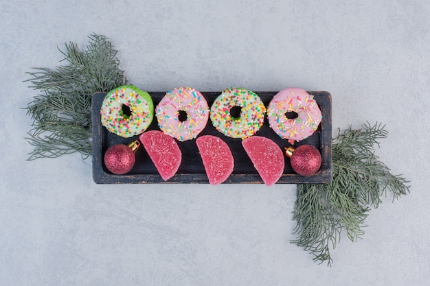 Foto grátis deliciosos donuts com sprinklers e marmeladas na placa preta.