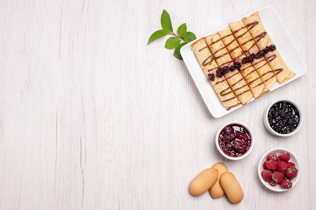 Deliciosos rolos de panqueca com geleia e biscoitos no fundo branco