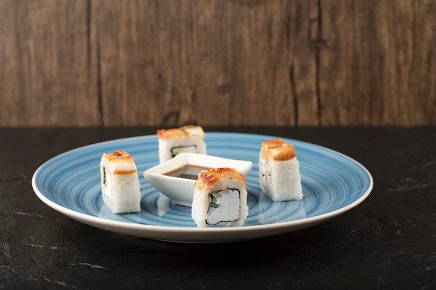 Deliciosos rolos de sushi de dragão e molho de soja no prato azul