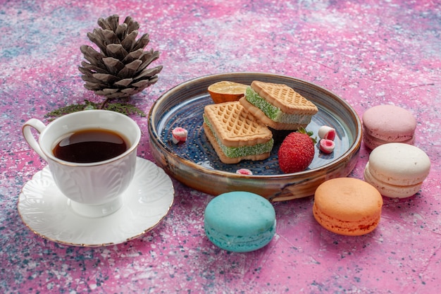 Deliciosos sanduíches de biscoito com deliciosos macarons franceses e uma xícara de chá na mesa rosa