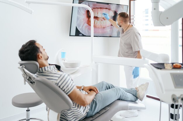 Dentista discutindo com paciente, mostrando a imagem de seus dentes na tela