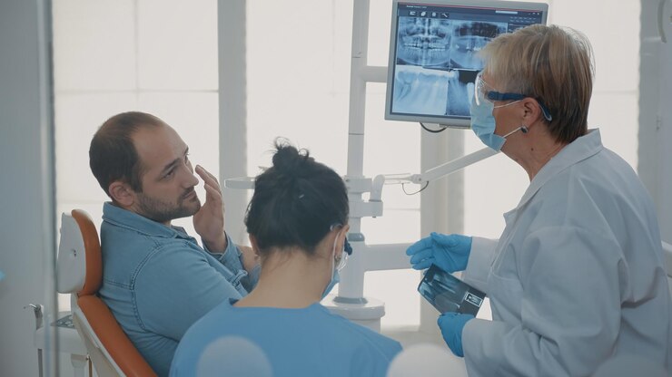 Foto grátis dentista e enfermeira explicando a varredura de raio x para paciente com dor de dente no gabinete de estomatologia. equipe de especialistas fazendo consulta de higiene bucal para tratar o homem com dor com problema de dentadura.