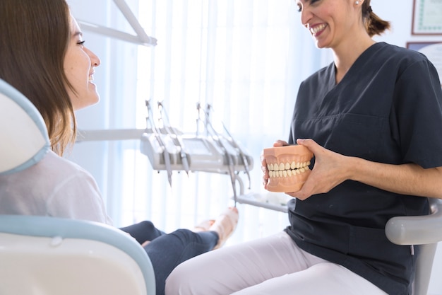 Dentista, explicando o paciente sobre modelo de dentes na clínica