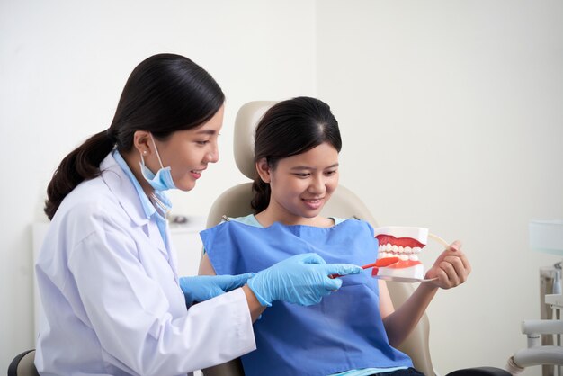 Dentista feminina asiática, demonstrando a técnica de escovação de dentes para paciente