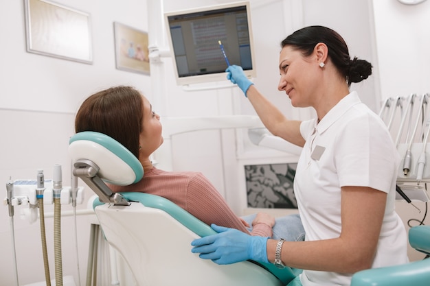 Dentista feminina educando seu paciente, trabalhando em sua clínica odontológica