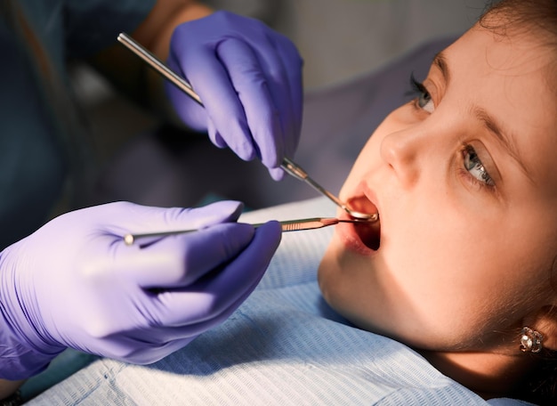 Dentista feminina examinando os dentes da menina no consultório odontológico