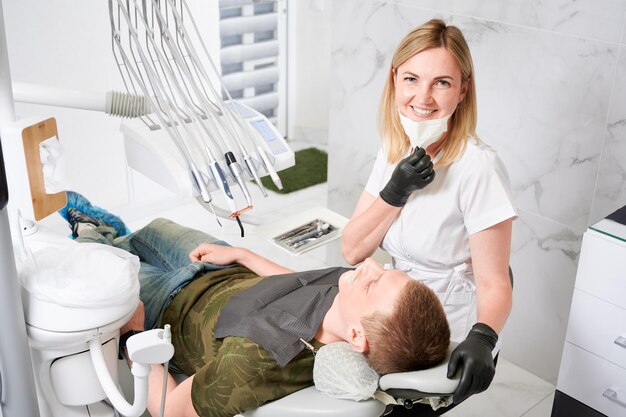 Dentista feminina no trabalho com paciente examinando seus dentes com instrumentos odontológicos