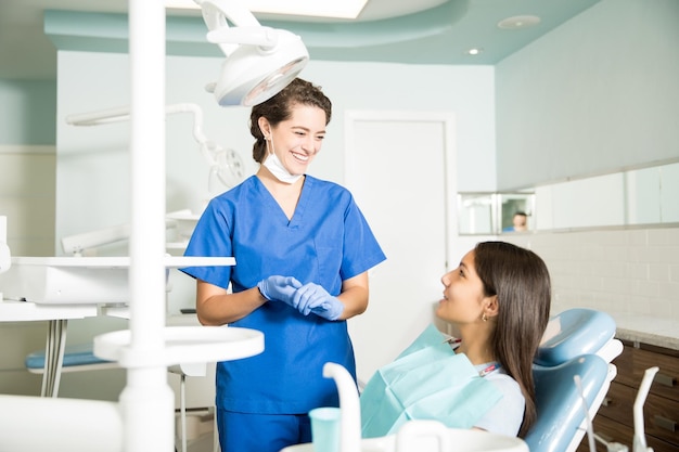 Dentista feminina sorridente de uniforme conversando com adolescente na clínica odontológica