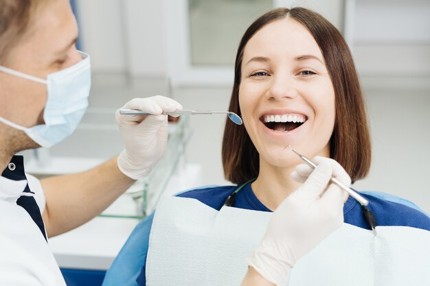 Dentista masculino, branco, examinando os dentes de uma jovem paciente na clínica odontológica