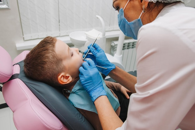 Dentista pediátrico trata cárie infantil e cavidade oral de menino sentado na cadeira do dentista durante check-up médico regular