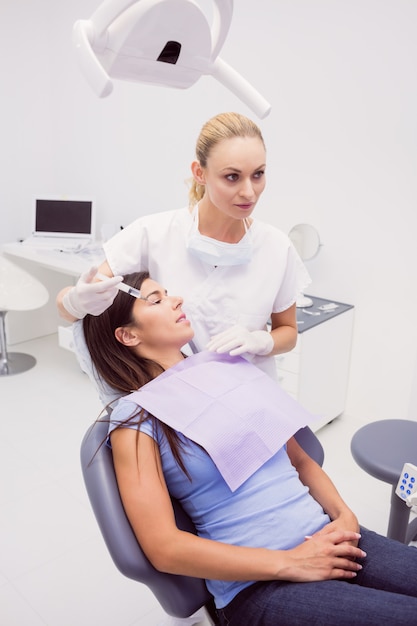 Dentista segurando uma seringa enquanto examina o paciente