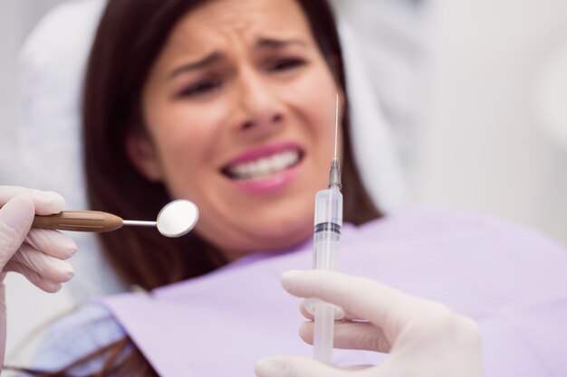 Dentista segurando uma seringa na frente do paciente assustado