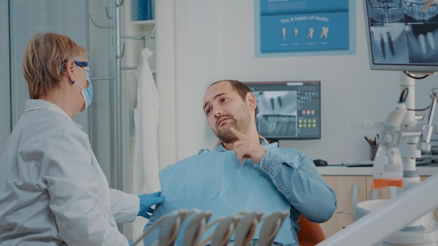 Dentista sênior examinando paciente com dor de dente grave, preparando-se para fazer consulta estomatológica com ferramentas odontológicas no gabinete. Médico tratando o homem com dor com problemas de higiene bucal.