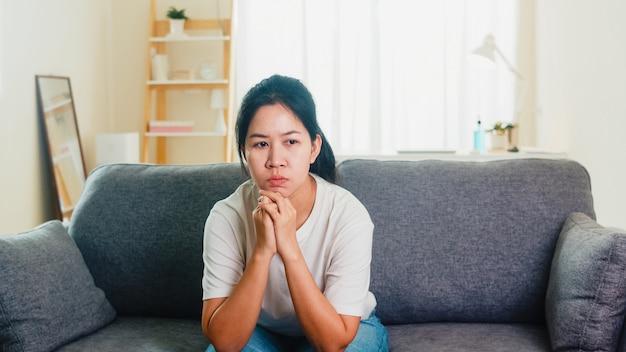 Deprimido chorando mulher asiática estressada com dor de cabeça, sentado no sofá na sala de estar em casa
