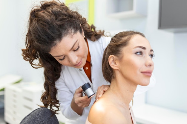 Dermatologista em luvas de látex segurando dermatoscópio enquanto examina paciente atraente com doença de pele dermatologista feminina examinando paciente com dermatoscópio procurando sinais de câncer de pele
