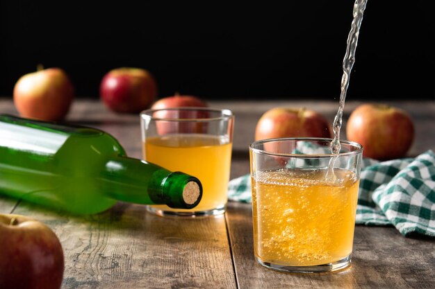 Derramando bebida de cidra de maçã em um copo na mesa de madeira