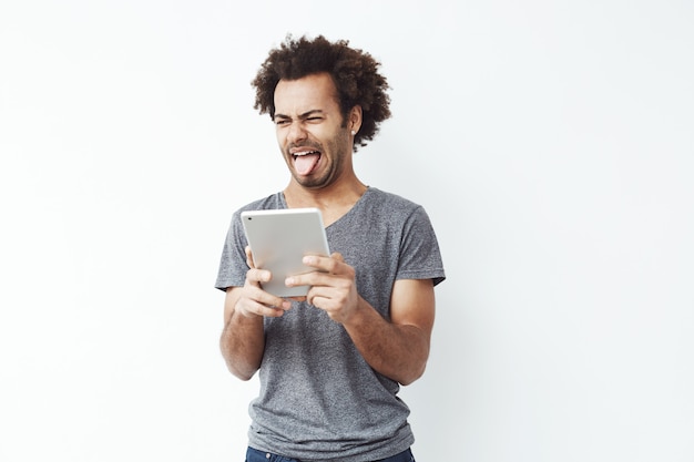 Foto grátis desagradou homem africano mostrando a língua segurando o tablet.