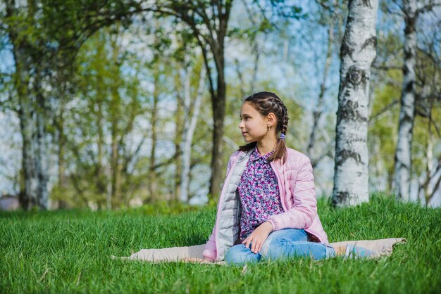 Descontraída menina sentada na grama e olhando para o lado