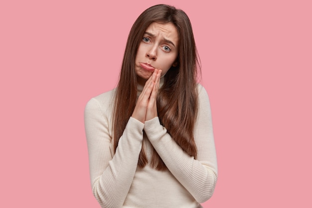 Desesperada, triste, jovem encantadora com cabelos longos, mantém as palmas das mãos em gesto de oração, pede a Deus para realizar os sonhos, implora por favor