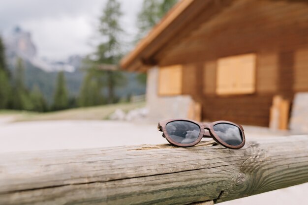 Desfoque a foto de uma casa de madeira na montanha na floresta com óculos de sol da moda em primeiro plano