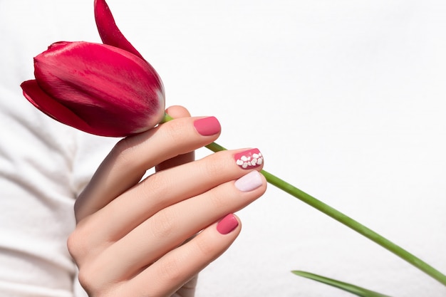 Design de unhas rosa. Mão feminina com manicure rosa segurando flor tulipa