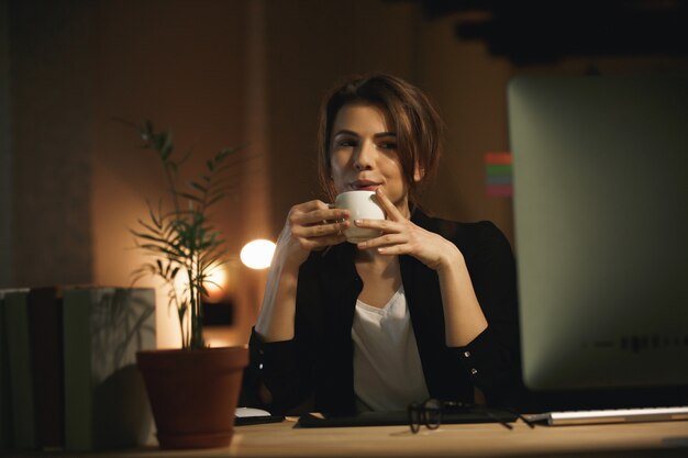 Designer de mulher jovem sério à noite usando o computador