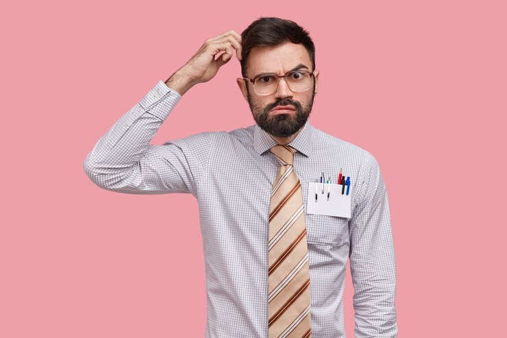 Foto grátis designer hesitante e inseguro coça a cabeça e olha com expressão séria, pensa em novo desenho, veste camisa formal, tem canetas e lápis no bolso